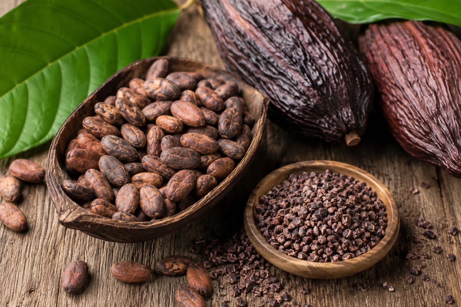 Boabe de cacao si cacao nibs in boluri din lemn, pe fundal natural, alaturi de pastai de cacao